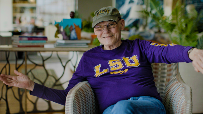 James Carville waiving hello wearing LSU sweatshirt. Movie Winning Is Everything Stupid